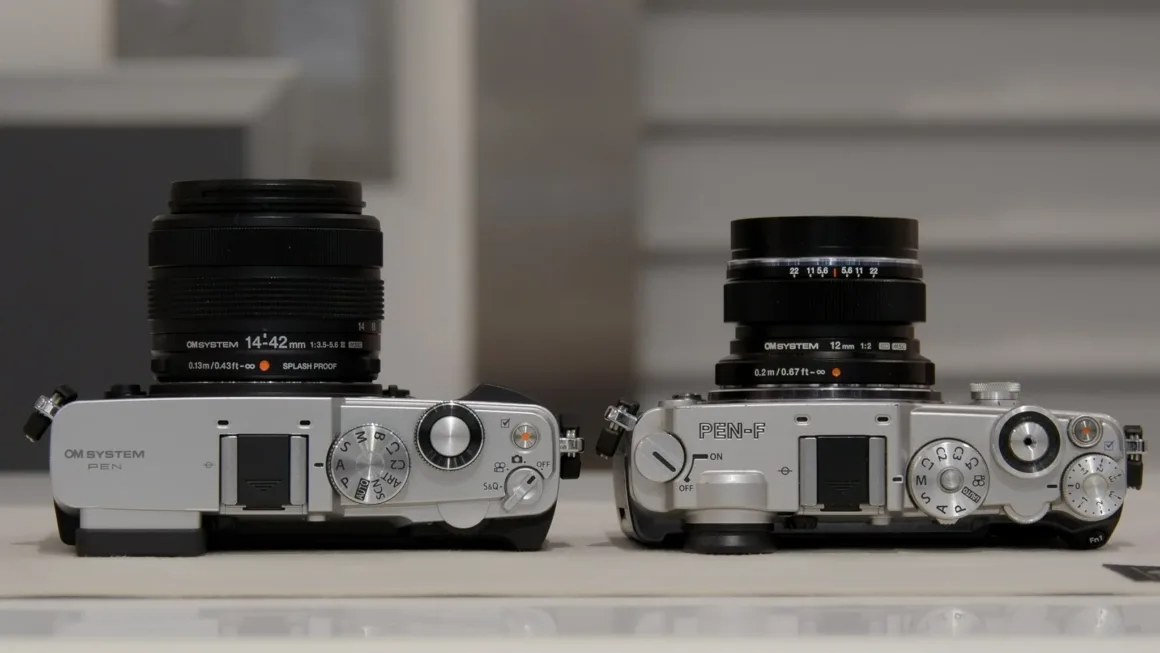 OM System PEN İncelemesi: Tanıdık Ama Son Derece Şık 20 Two silver mirrorless cameras sit side-by-side on a white surface, each equipped with a black lens.
