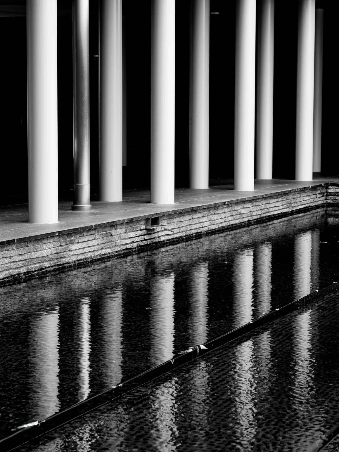 OM System PEN İncelemesi: Tanıdık Ama Son Derece Şık 44 A row of white cylindrical columns stands beside a dark reflecting pool, with the pillars mirrored in the rippling water.