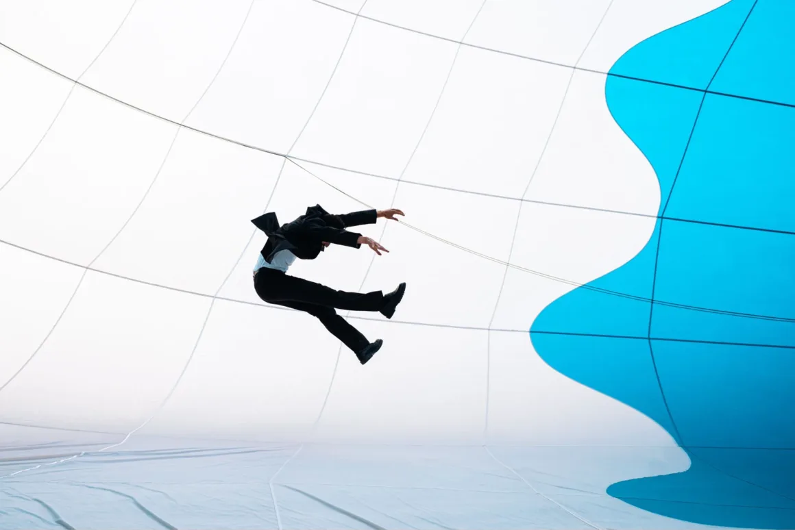 A person in a dark suit jumps mid-air against a white and blue grid-patterned background.