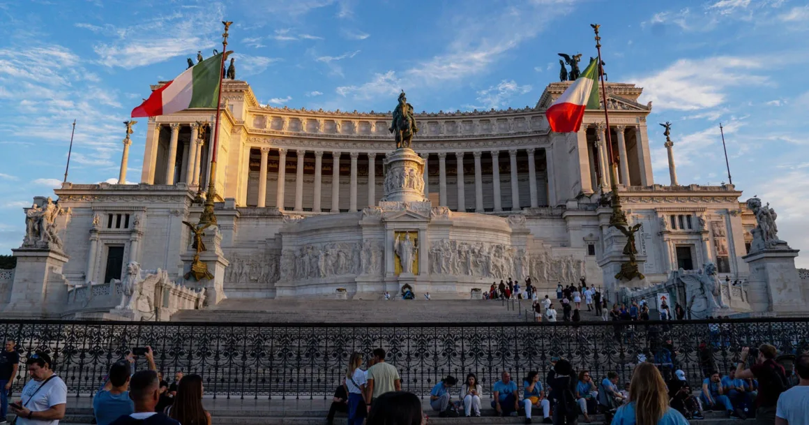 Roma’daki beyaz mermer Vittorio Emanuele II Anıtı, atlı heykel, İtalyan bayrakları ve merdivenlerdeki ziyaretçilerle görülüyor.