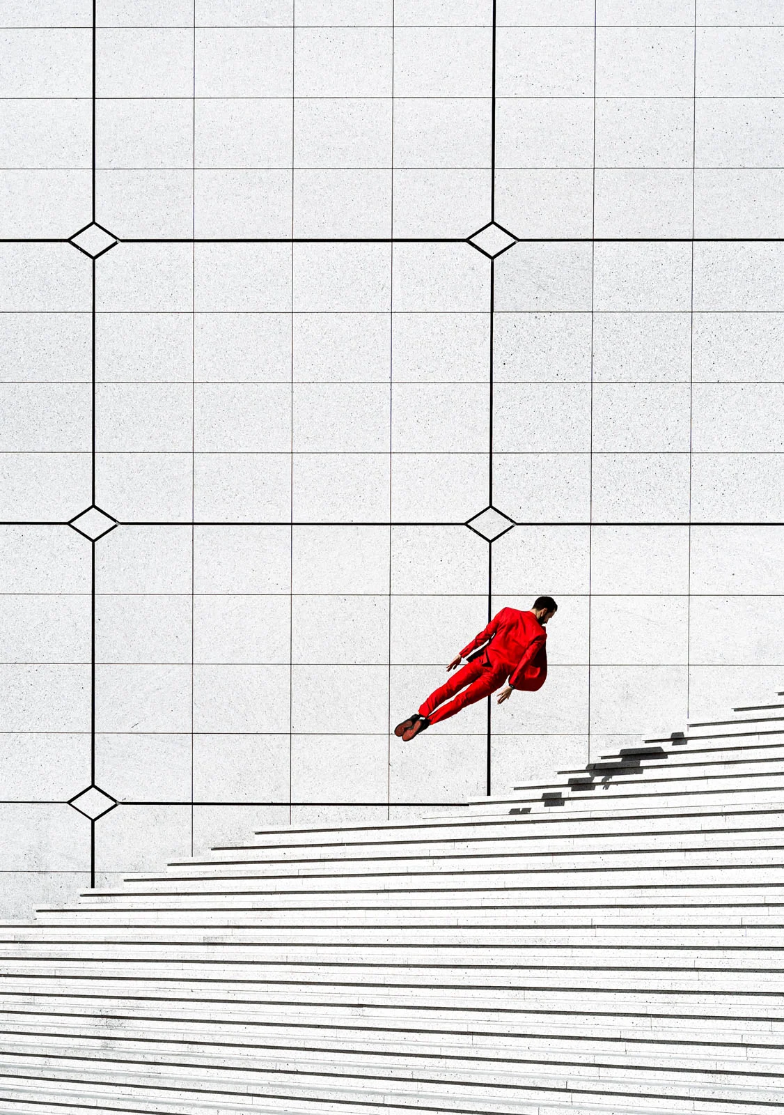 A person in a bright red suit appears to be floating horizontally above a set of wide, white concrete stairs against a tiled wall.