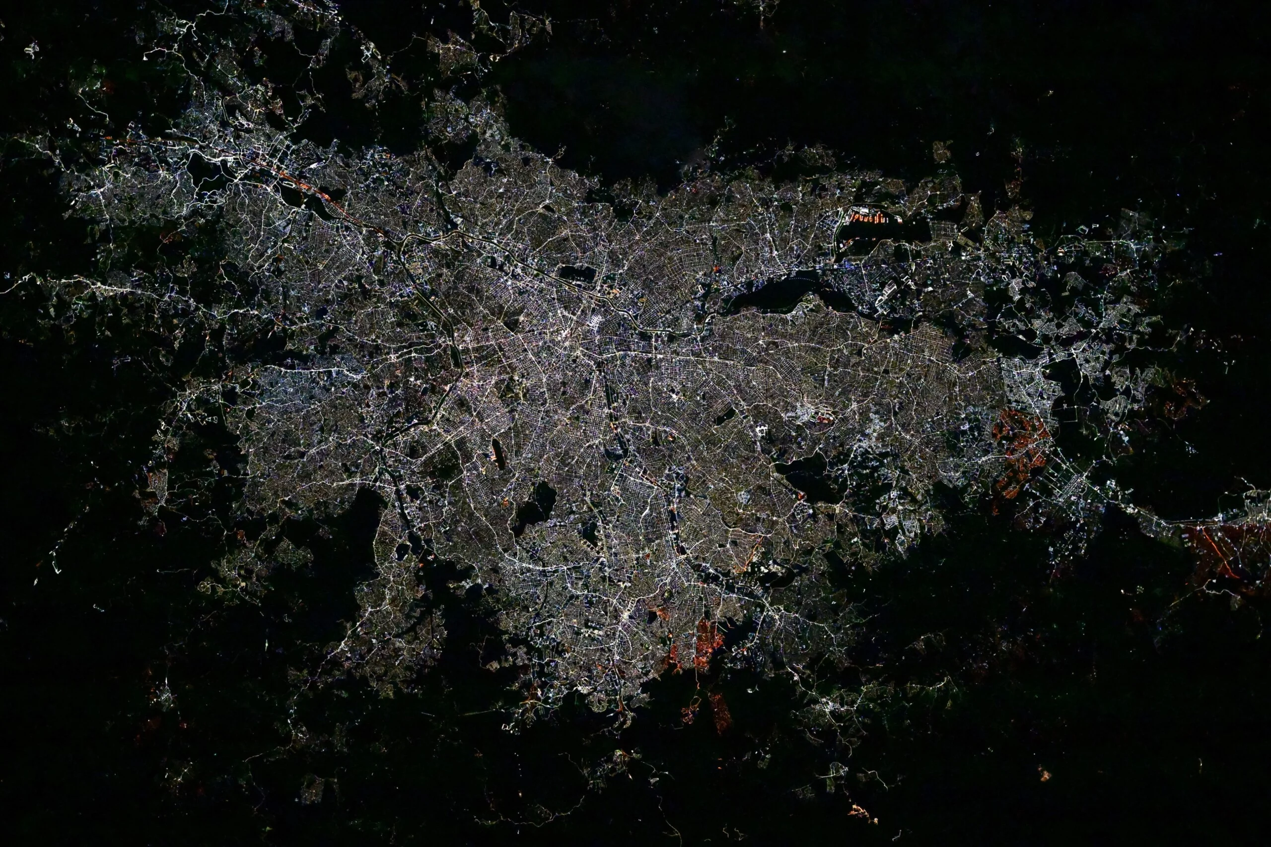 Astronotun Önce-Sonra Fotoğrafları Kentlerin Turuncudan Beyaz Işığa Geçişini Gösteriyor 24 An overhead night view of a sprawling, densely lit city grid surrounded by dark, unlit natural terrain.