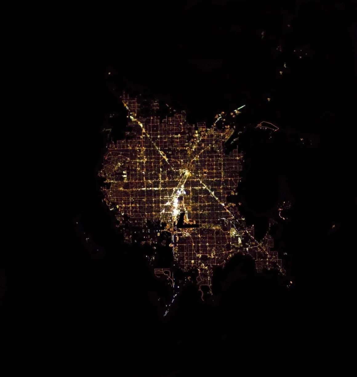 Astronotun Önce-Sonra Fotoğrafları Kentlerin Turuncudan Beyaz Işığa Geçişini Gösteriyor 27 An aerial night view of a city grid illuminated by streetlights, showing a dense cluster of lights surrounded by darkness.
