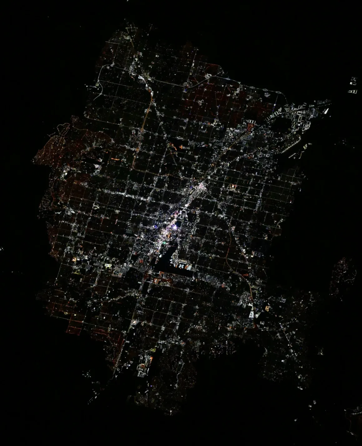 Astronotun Önce-Sonra Fotoğrafları Kentlerin Turuncudan Beyaz Işığa Geçişini Gösteriyor 28 An aerial night view of a city grid illuminated by streetlights and buildings, surrounded by dark, undeveloped land.