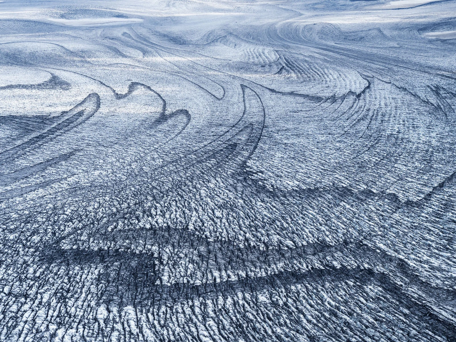 Natural Landscape Photography Awards 2026’nın Kazananları Açıklandı 76 An aerial view of a glacier surface featuring intricate, dark, swirling patterns of debris and deep crevasses across the ice.