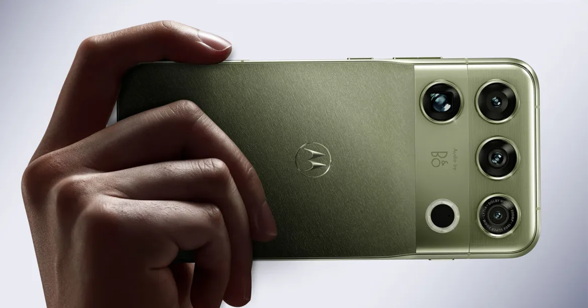 A hand holds a green smartphone with a triple-lens camera system and a Motorola logo on the back.