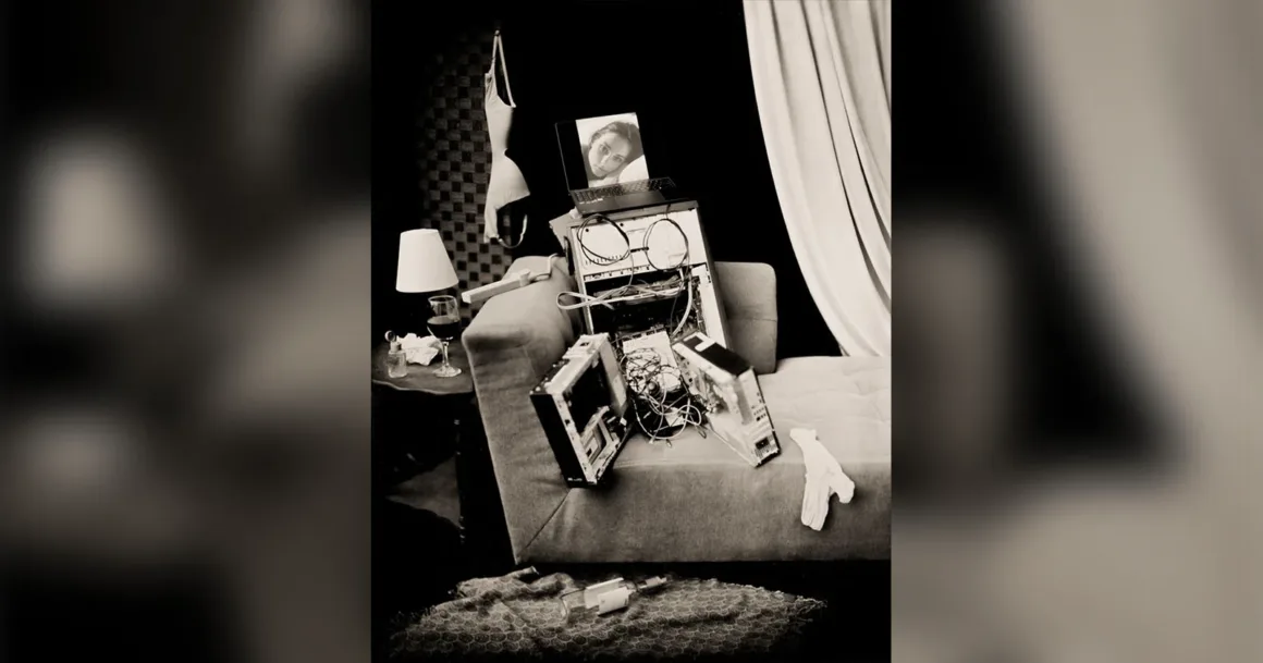 Yapay Zekâ Sohbet Botları İkilemi 18 Yapay zekâ sohbet botları, yalnızlık ve yakınlık arayışımızı nasıl değiştiriyor? Fotoğrafçı Shane Balkowitsch, sahte görüntülerden sanal ilişkilere uzanan dönüşümü ve insan kalmanın anlamını sorguluyor.
Bir kanepenin üzerinde parçalarına ayrılmış bir bilgisayar kasası ve üzerinde ekranında bir kadının yüzünün göründüğü dizüstü bilgisayar; yakındaki duvarda ise bir sütyen asılı.