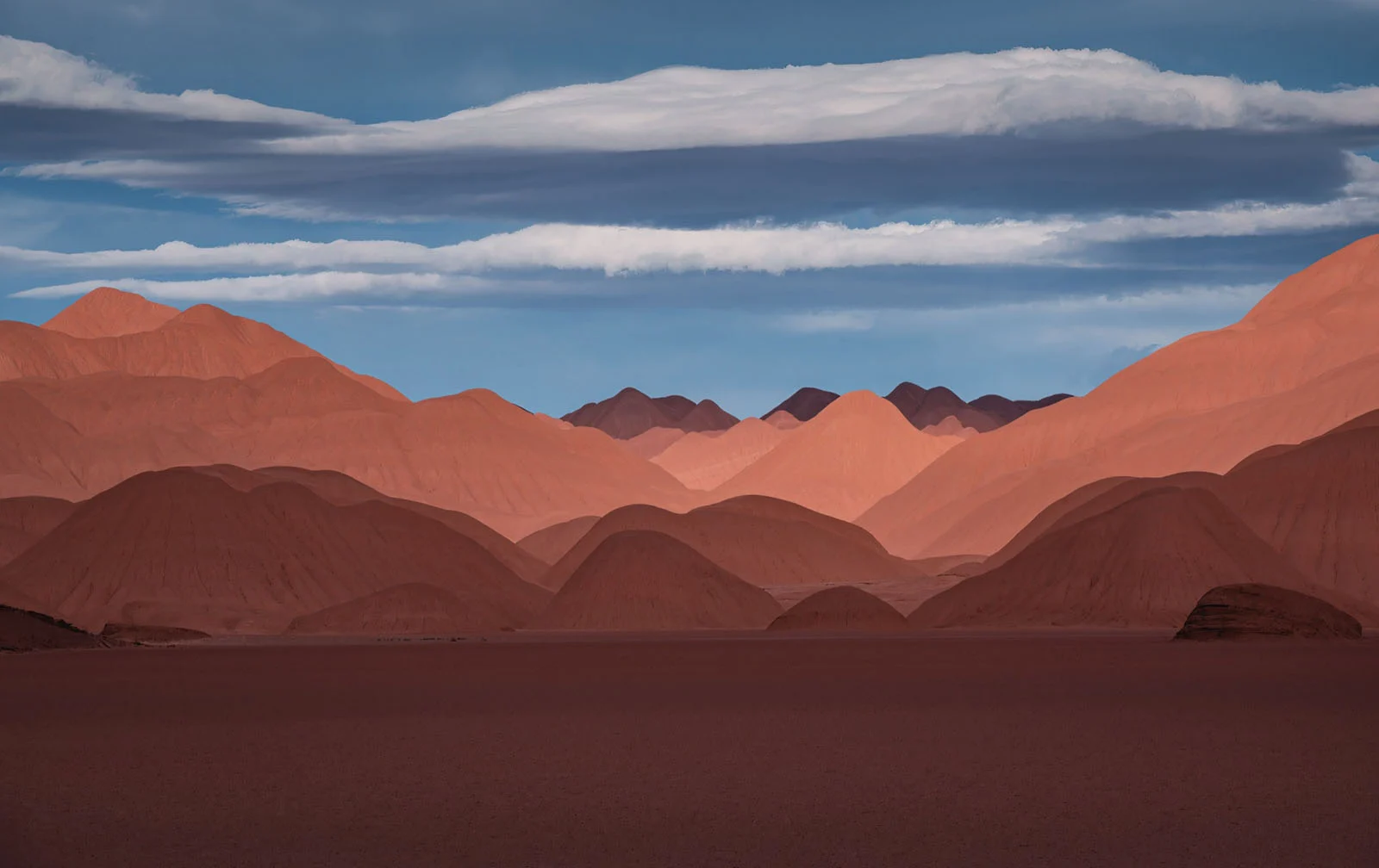 Natural Landscape Photography Awards 2026’nın Kazananları Açıklandı 71 A vast, flat desert landscape stretches toward a series of layered, reddish-brown mountain peaks under a blue sky with horizontal clouds.