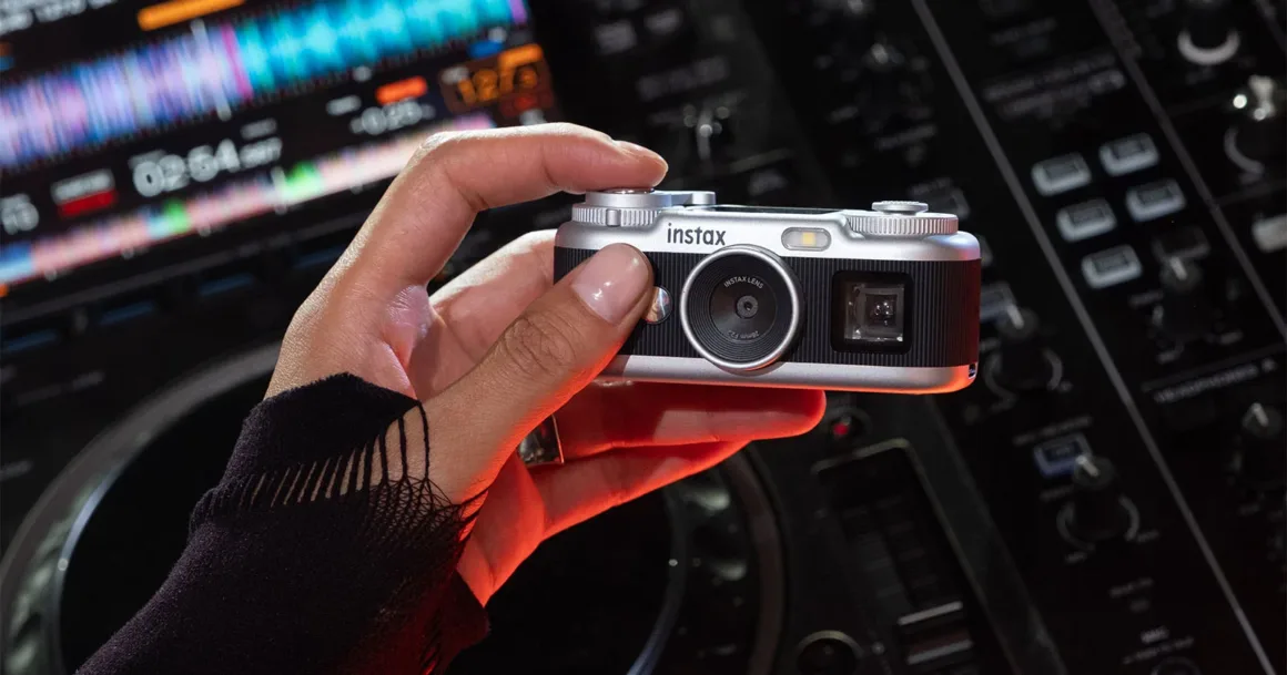 Fujifilm Instax Pal 2, Tuhaf Selefinden Tamamen Farklı Görünüyor 22 Siyah kollu bir el, DJ mikserinin önünde gümüş-siyah Instax kamerayı tutuyor.