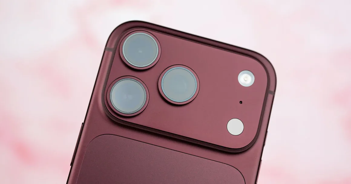 Apple, iPhone 18 Pro’daki Değişken Diyaframı Anlatıyor 19 Koyu kırmızı akıllı telefonun arkasındaki üç yuvarlak objektif, flaş ve küçük sensörden oluşan yükseltilmiş kamera modülünün yakın planı.