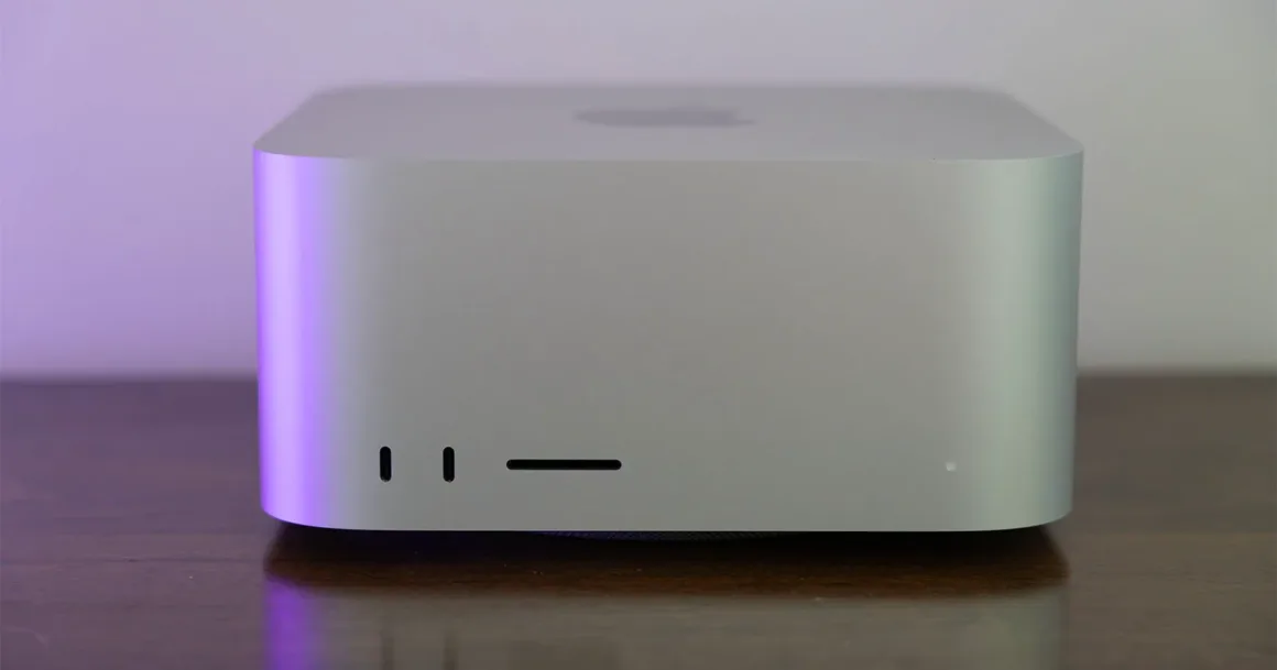 Ahşap yüzey üzerinde duran, önündeki iki USB-C bağlantısı, SD kart yuvası ve durum ışığı görülen gümüş Apple Mac Studio