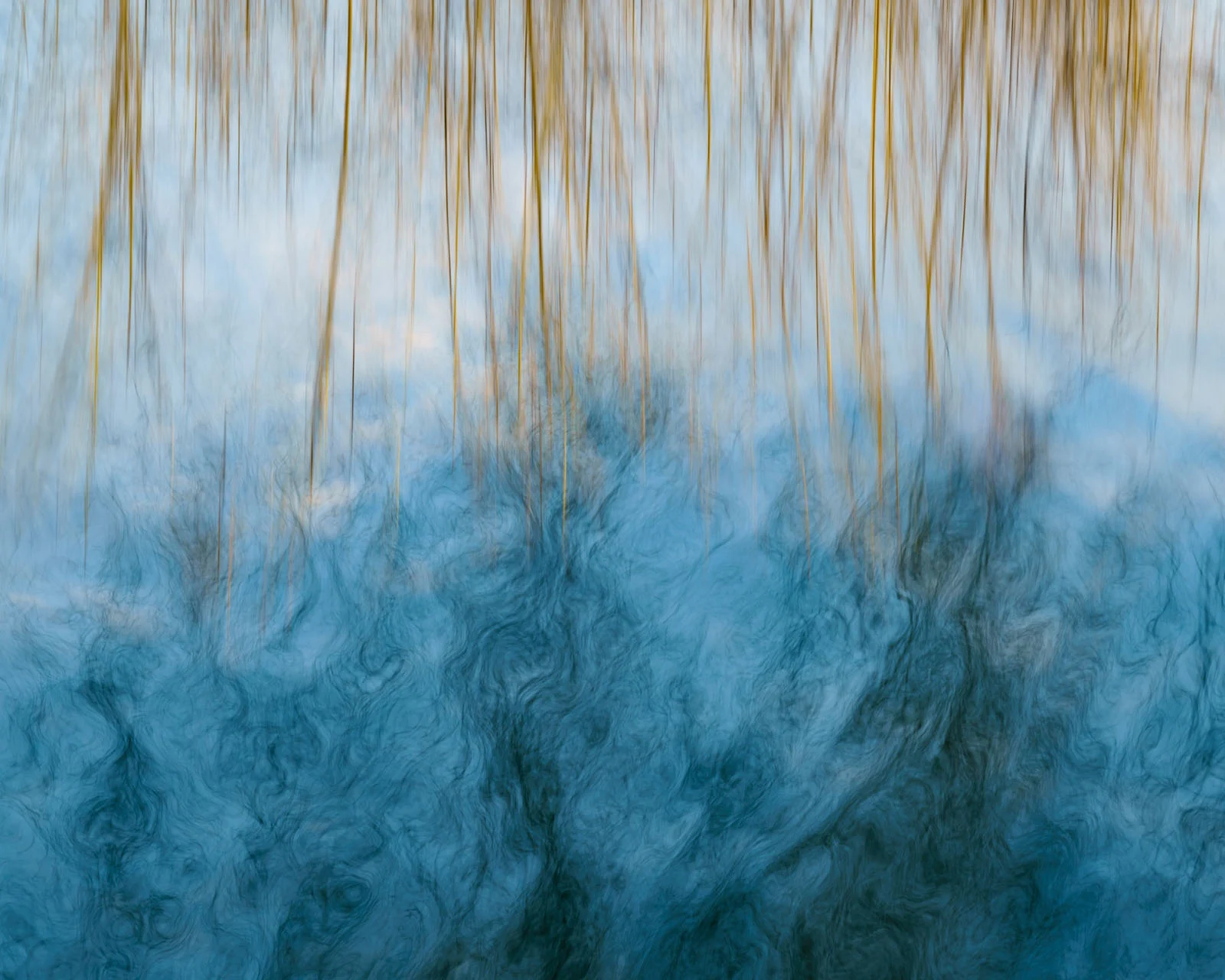 Natural Landscape Photography Awards 2026’nın Kazananları Açıklandı 87 Vertical golden reeds hang over a blurred, swirling blue water surface reflecting the sky.