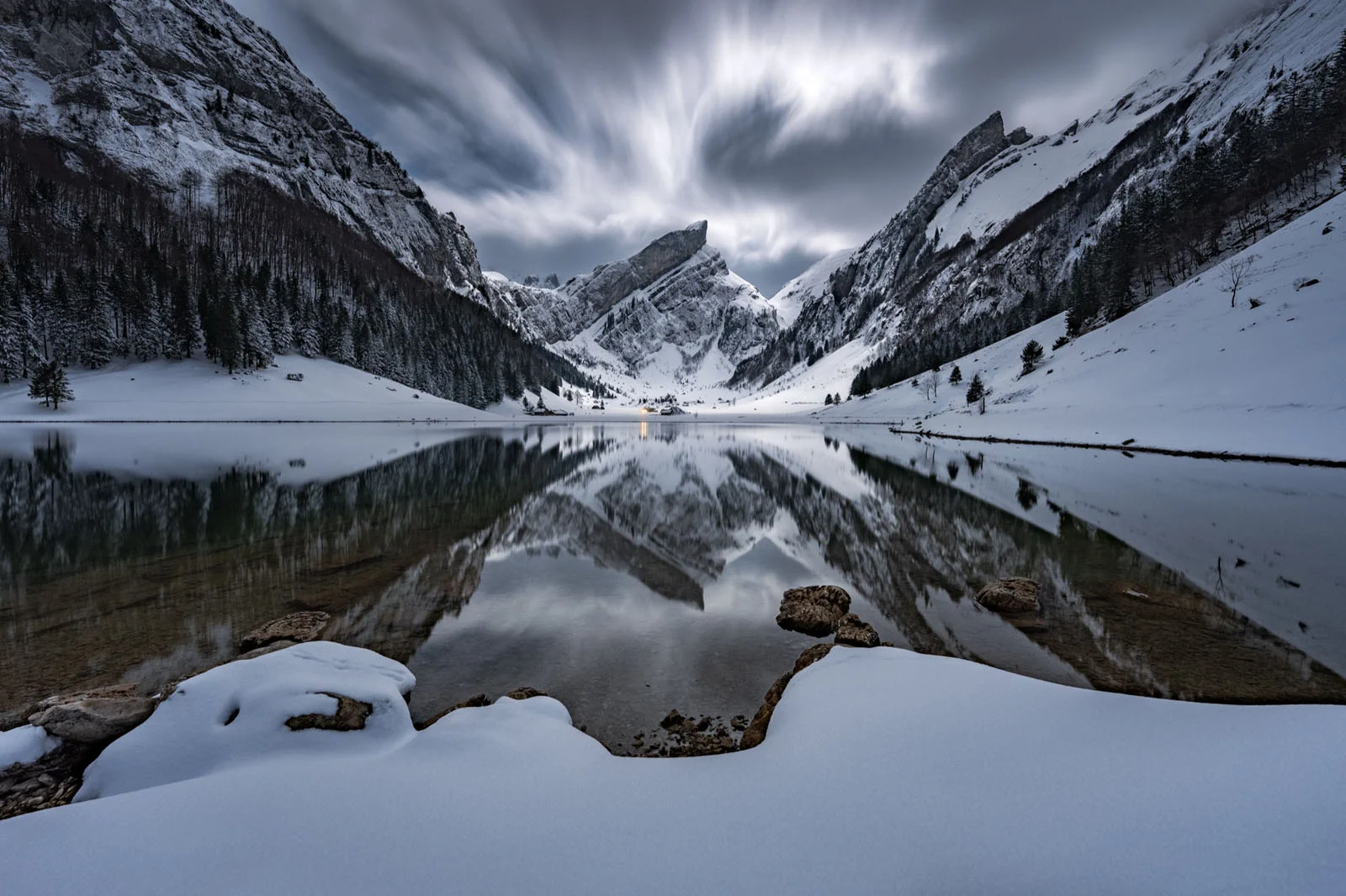 Natural Landscape Photography Awards 2026’nın Kazananları Açıklandı 89 A snow-covered mountain range reflects perfectly in the still, dark water of a lake under a dramatic, cloudy sky.