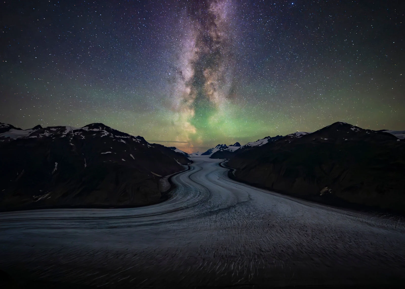 Natural Landscape Photography Awards 2026’nın Kazananları Açıklandı 88 A winding glacier flows between dark, snow-capped mountain ranges under a vibrant night sky filled with the Milky Way.