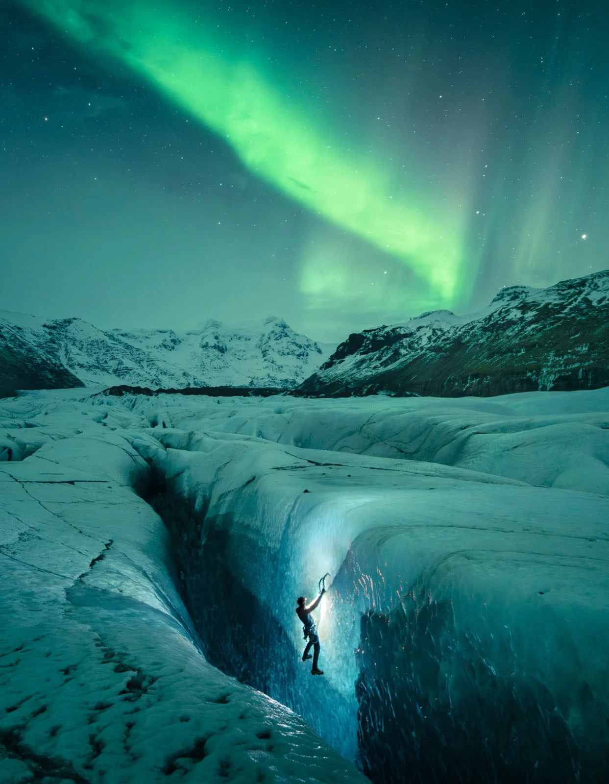 Natural Landscape Photography Awards 2026’nın Kazananları Açıklandı 90 A climber uses an ice axe to scale a vertical wall of a glacier crevasse under a vibrant green aurora borealis.