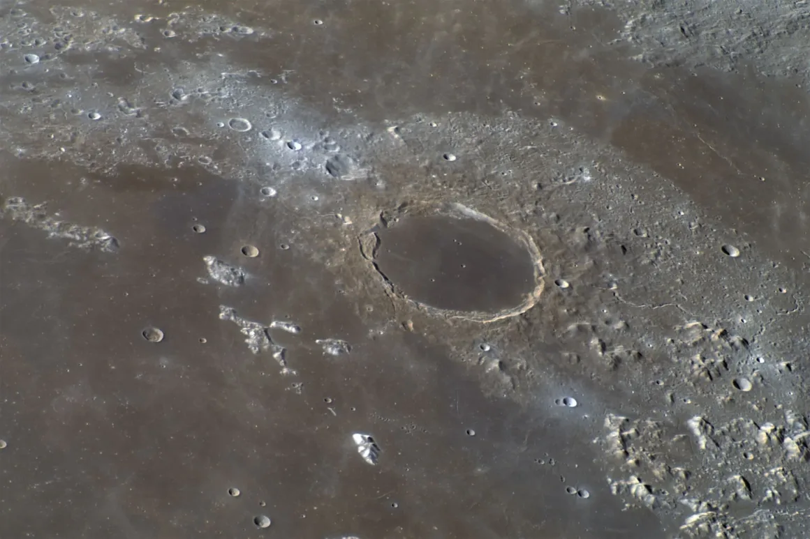 Astronomy Photographer of the Year 2026: Bu Dünyadan Olmayan 31 Kazanan 28 A high-angle view of the lunar surface featuring a large, smooth-floored impact crater surrounded by smaller craters and rugged terrain.