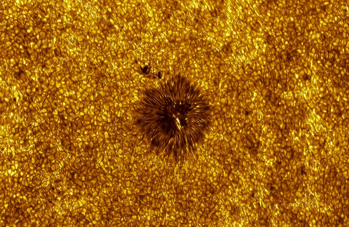 Astronomy Photographer of the Year 2026: Bu Dünyadan Olmayan 31 Kazanan 30 A high-resolution view of the Sun's surface showing a dark sunspot surrounded by a granular, golden-yellow photosphere.