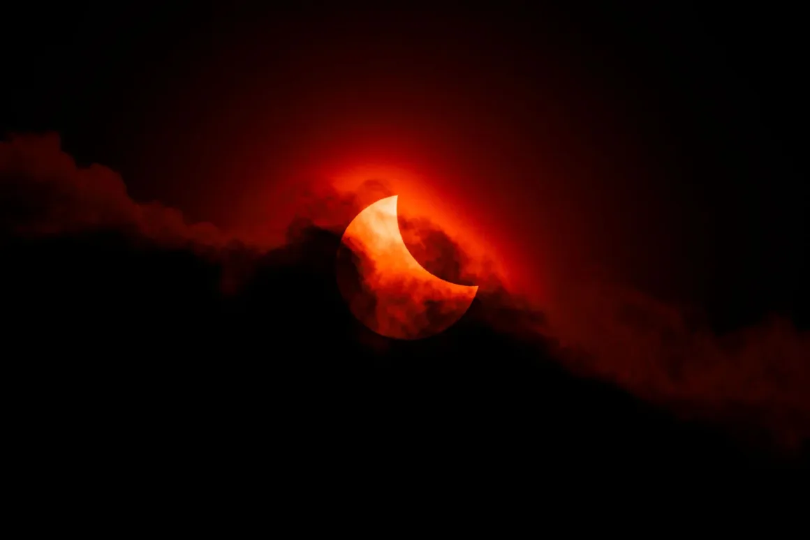 Astronomy Photographer of the Year 2026: Bu Dünyadan Olmayan 31 Kazanan 32 A crescent sun partially obscured by dark, red-tinted clouds against a black sky.