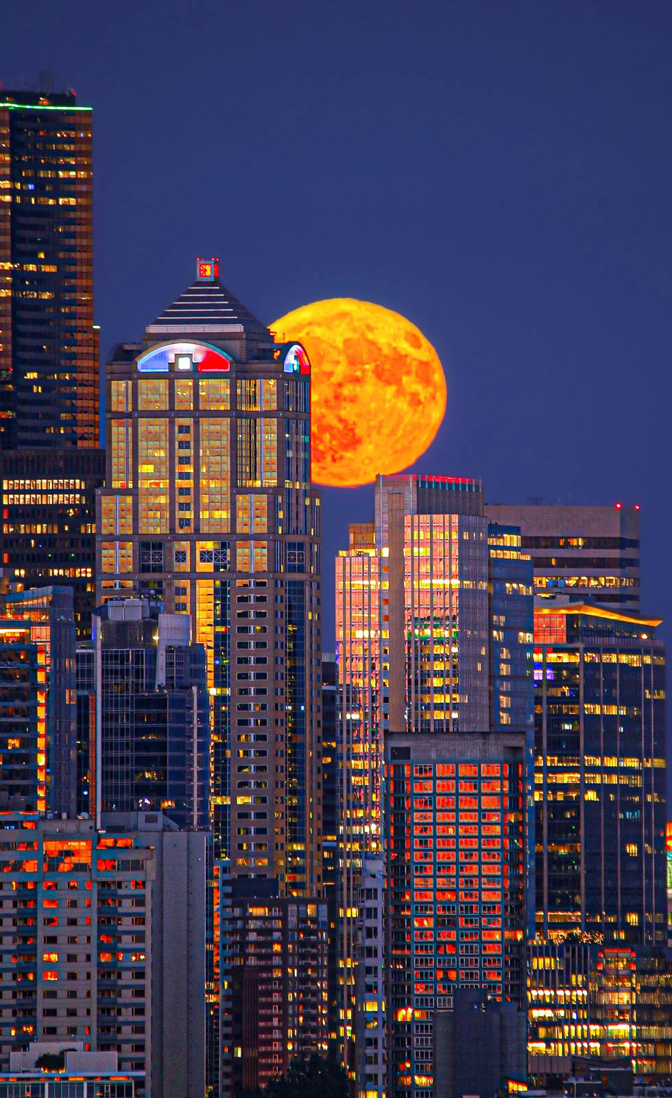 Astronomy Photographer of the Year 2026: Bu Dünyadan Olmayan 31 Kazanan 35 A large, orange full moon rises behind a dense cluster of illuminated skyscrapers at twilight.