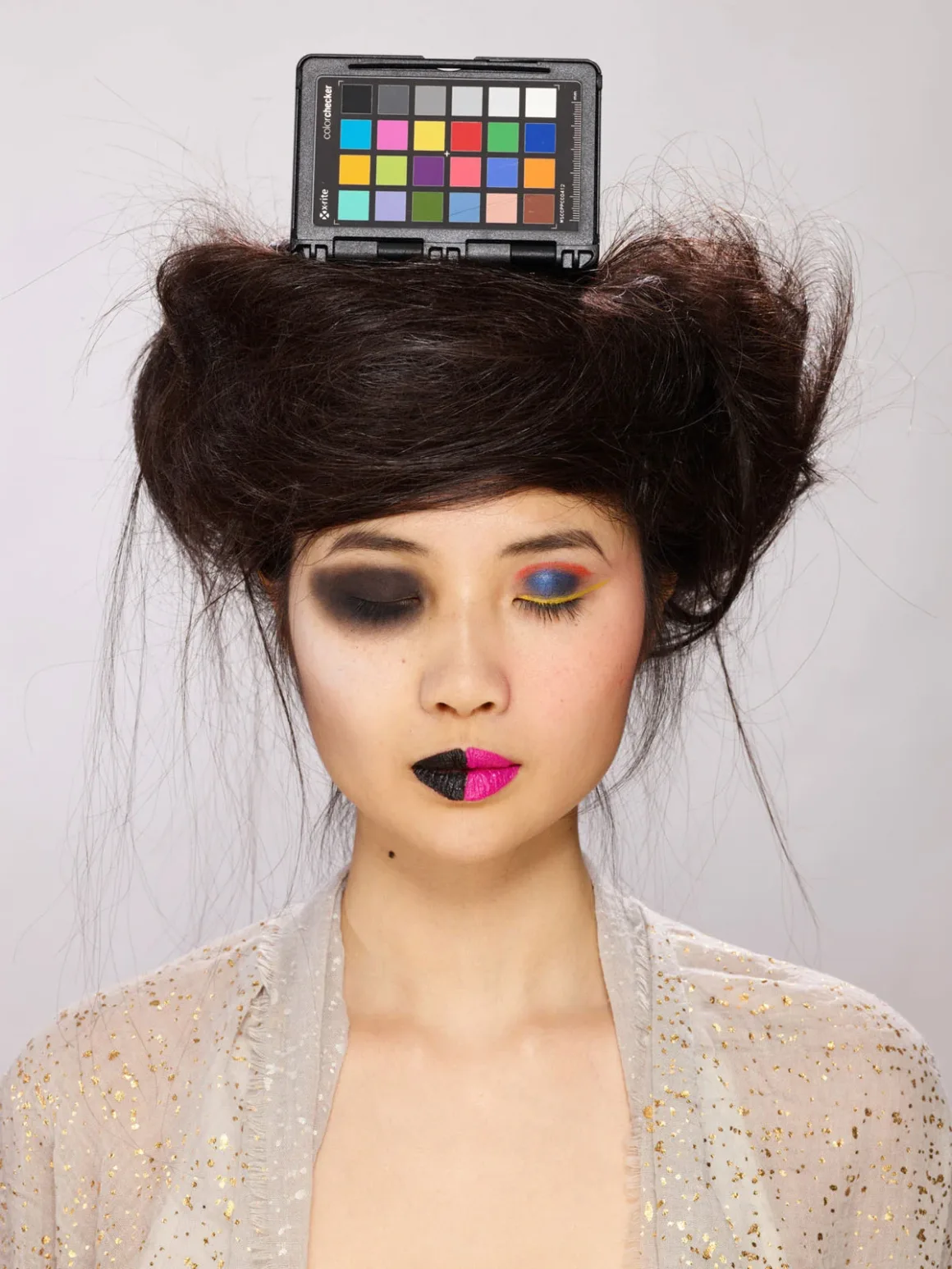Fotoğrafçıların Renkli Dostu ColorChecker 50 Yaşında 17 Gür siyah saçlı bir kişi, yüzünün bir yarısında siyah diğer yarısında canlı renkli makyajla başında bir renk kontrol kartı taşıyor.