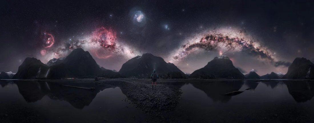 Epson International Pano Awards 2026 Kazananları Açıklandı 19 Bir kişi, yıldızlarla dolu canlı gece gökyüzünün altında dağ sırasına bakarak iki su kütlesi arasındaki kayalık kıyıda duruyor.