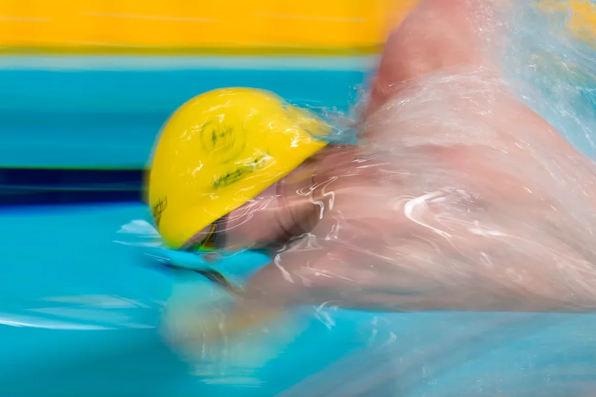 Glasgow 2026’da Bir Spor Fotoğrafçısının Çantasında Neler Vardı? 19 Parlak sarı bone takan bir yüzücü serbest stil yüzerken mavi havuz suyunda yoğun sıçramalar oluşturuyor.