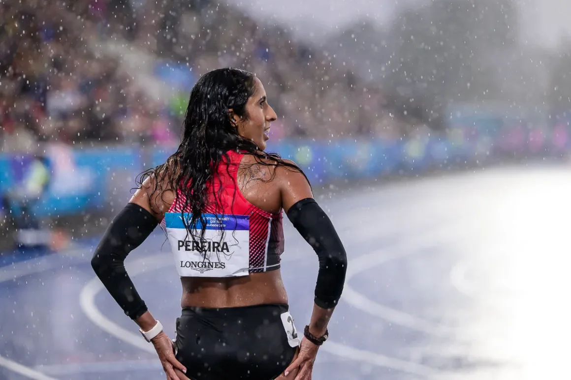 Glasgow 2026’da Bir Spor Fotoğrafçısının Çantasında Neler Vardı? 32 Uzun ıslak saçlı kadın atlet, yağmur altında pistte PEREIRA yazılı kırmızı forma ve siyah kol kolluklarıyla duruyor.