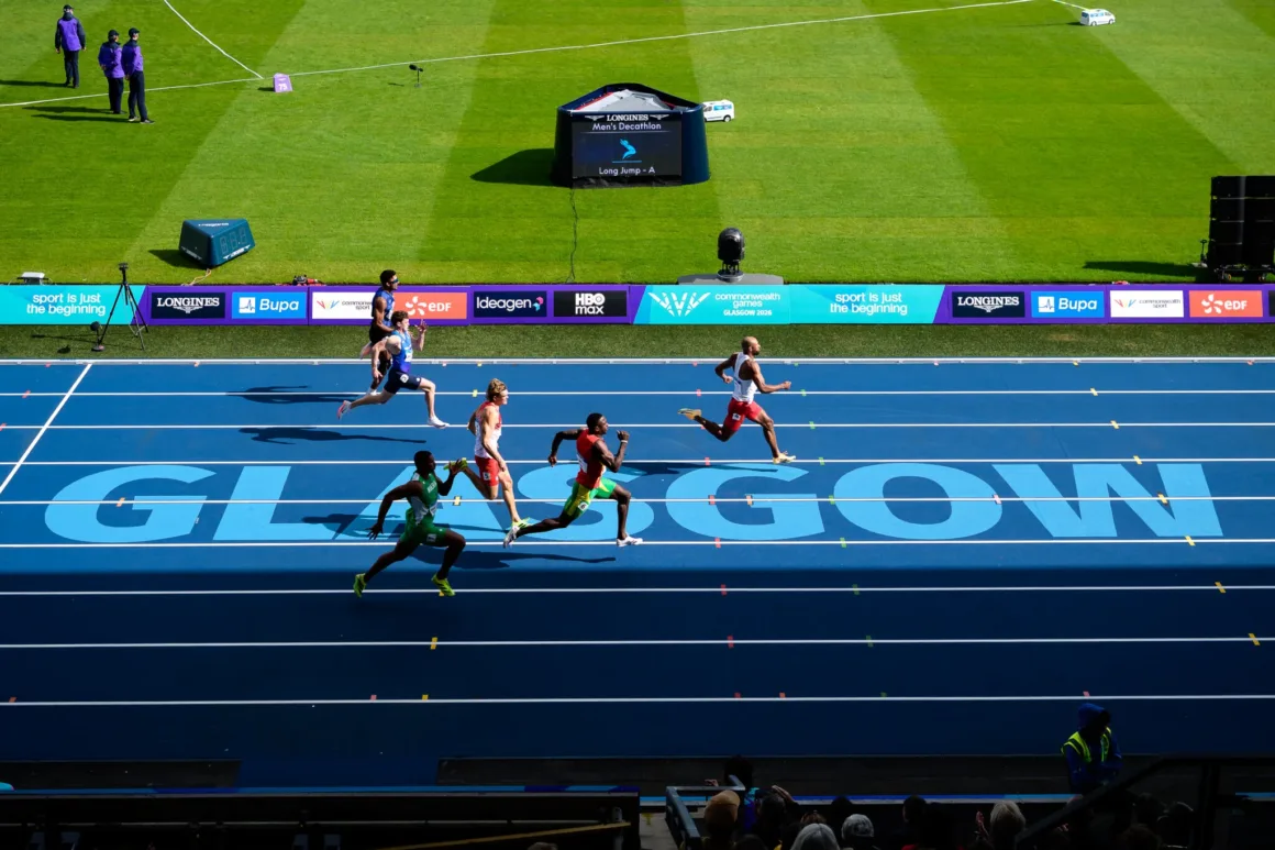 Glasgow 2026’da Bir Spor Fotoğrafçısının Çantasında Neler Vardı? 33 Atletler mavi pistte yarışırken zeminde büyük GLASGOW yazısı, dijital ekranda ise Men's Decathlon ifadesi görülüyor.