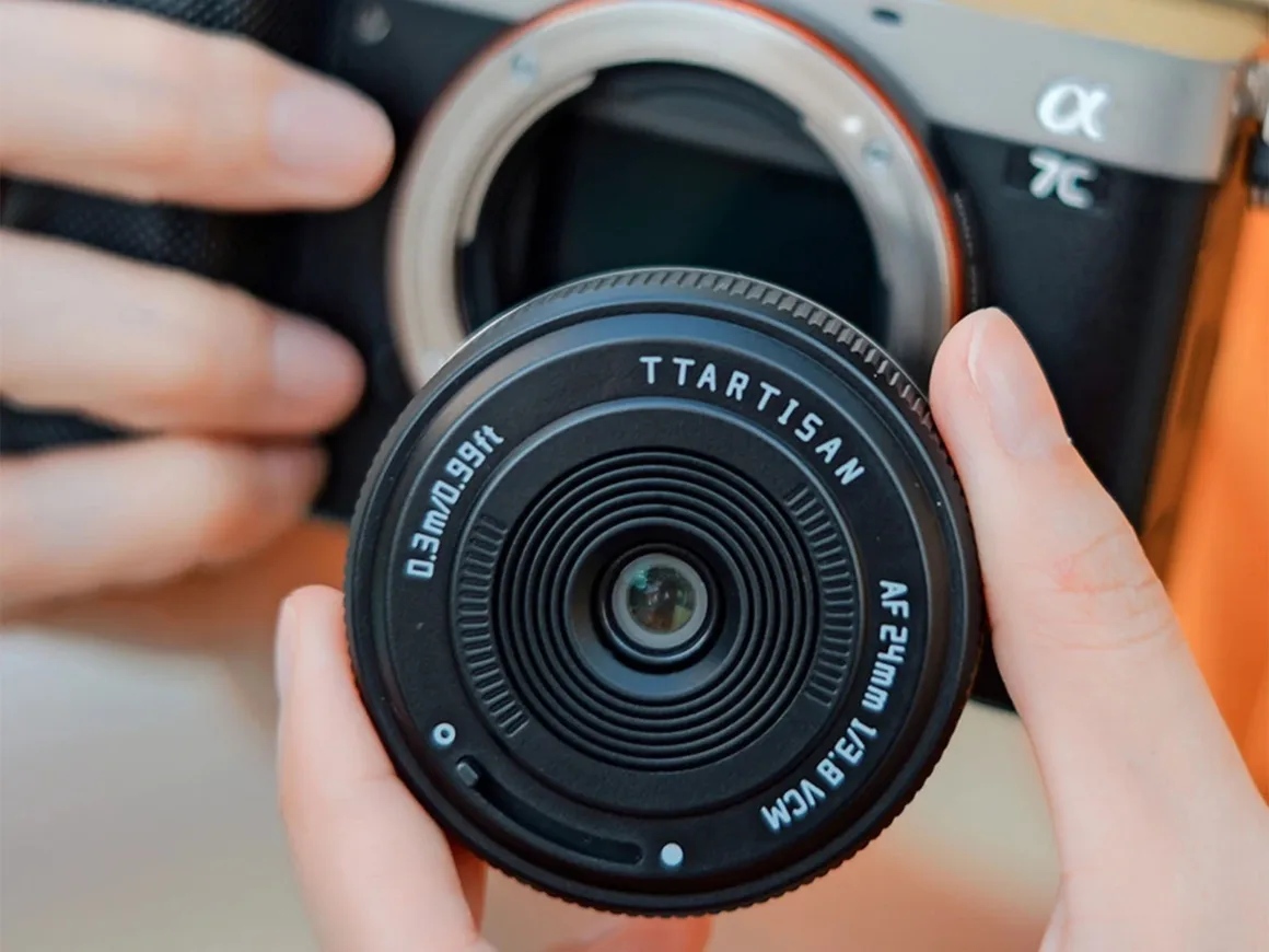 TTArtisan AF 24mm f/3.8 Mini: Sony E Mount için 57 Gramlık Pancake Objektif 21 Bir kişi, TTArtisan AF 24mm f/3.8 VCM objektifi Sony Alpha 7C fotoğraf makinesi gövdesinin önünde tutuyor.