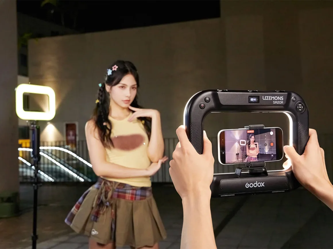 Godox Litemons SR20R, Telefon ve Gimbal Kameralar için RGB Işık Sunuyor 19 Bir kişi, ortasına akıllı telefon yerleştirilmiş Godox Litemons SR20R ışığı tutarak sarı atlet ve pileli etek giyen genç bir kadını çekiyor.
