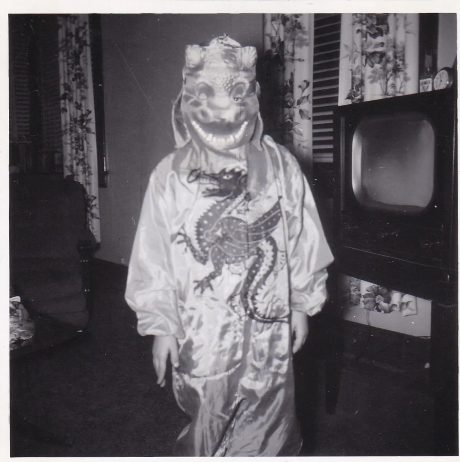20. Yüzyıl Ortalarından Tekinsiz Halloween Fotoğrafları 27 Ejderha maskesi ve kostümü giyen çocuk eski televizyonun bulunduğu bir oturma odasında duruyor