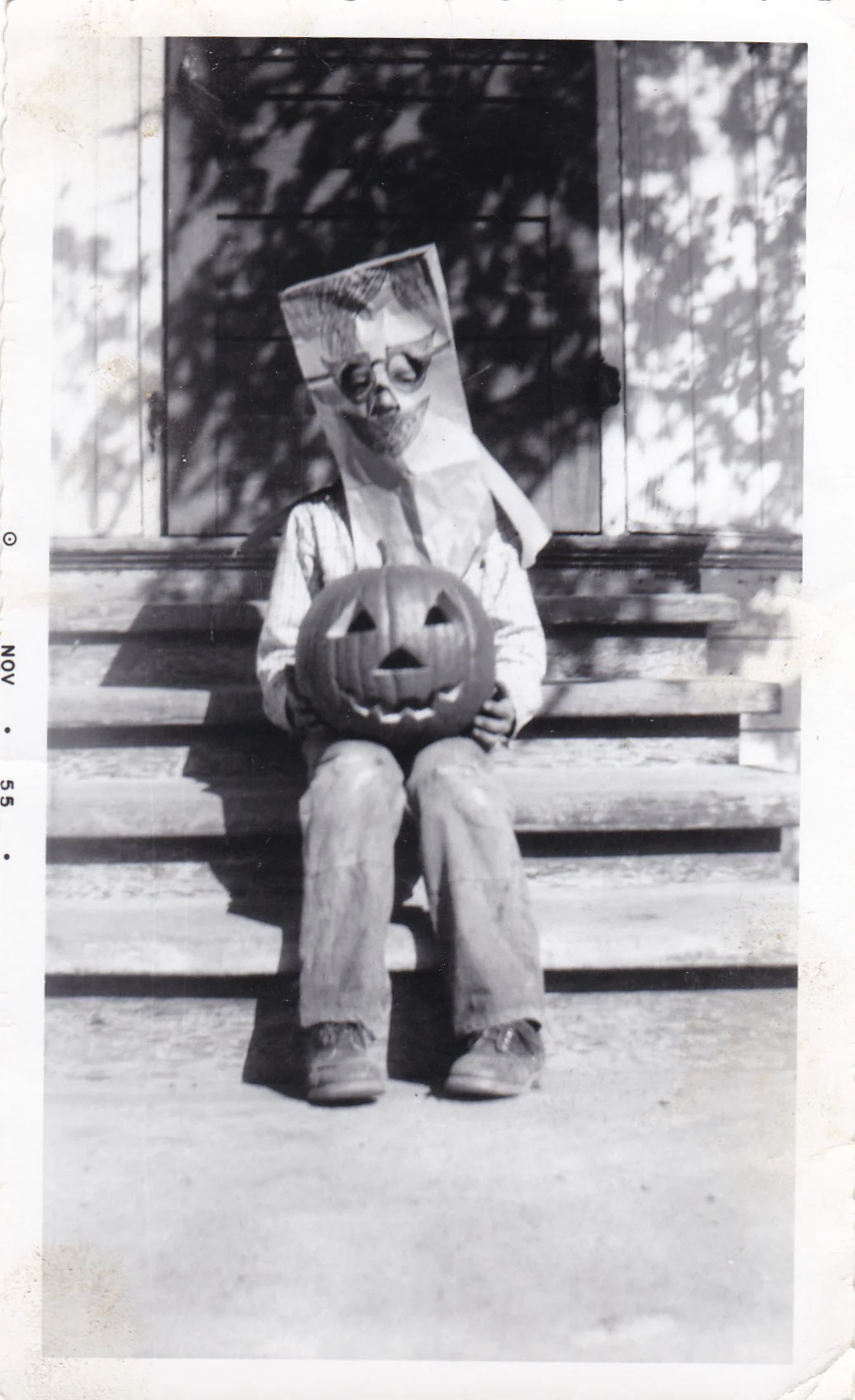 20. Yüzyıl Ortalarından Tekinsiz Halloween Fotoğrafları 26 Üzerine yüz çizilmiş kâğıt torba maskesi takan çocuk, oyulmuş balkabağıyla veranda basamaklarında oturuyor