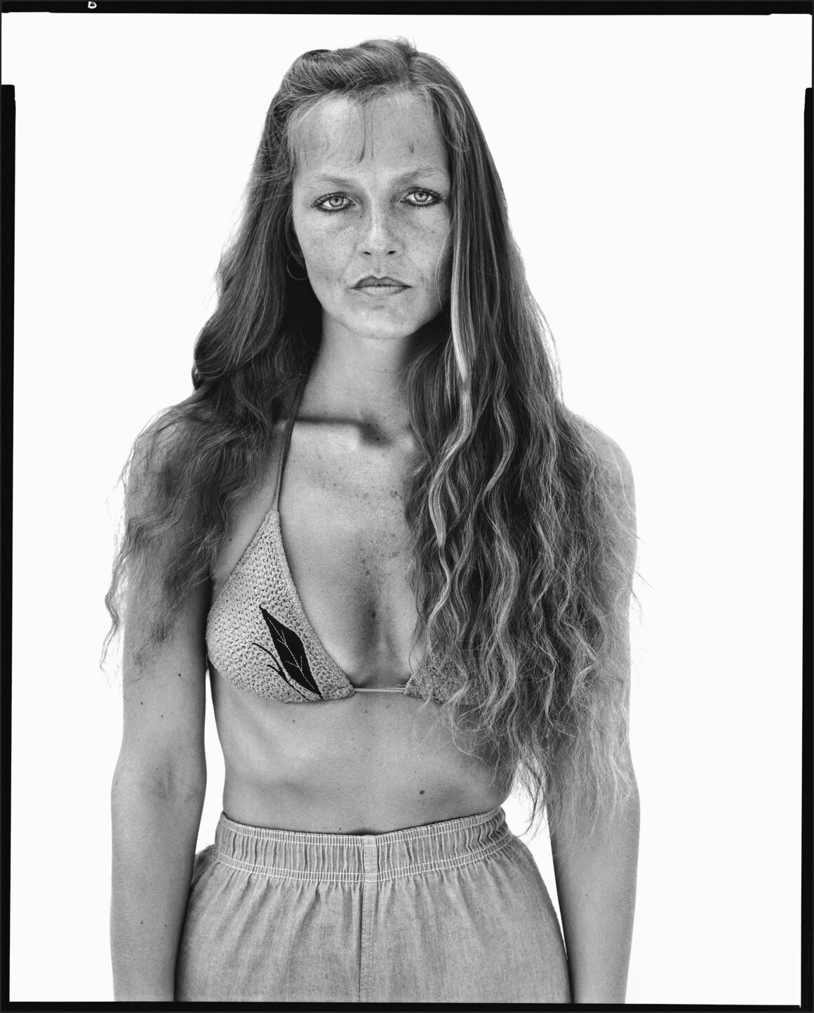 Richard Avedon’ın Amerika’nın Batısına Baktığı Portreler Londra’da 20 Uzun dalgalı saçlı bir kadın sade beyaz fon önünde duruyor. Yaprak desenli bikini üstü ve bağcıklı pantolon giyen kadın kameraya nötr bir ifadeyle bakıyor.