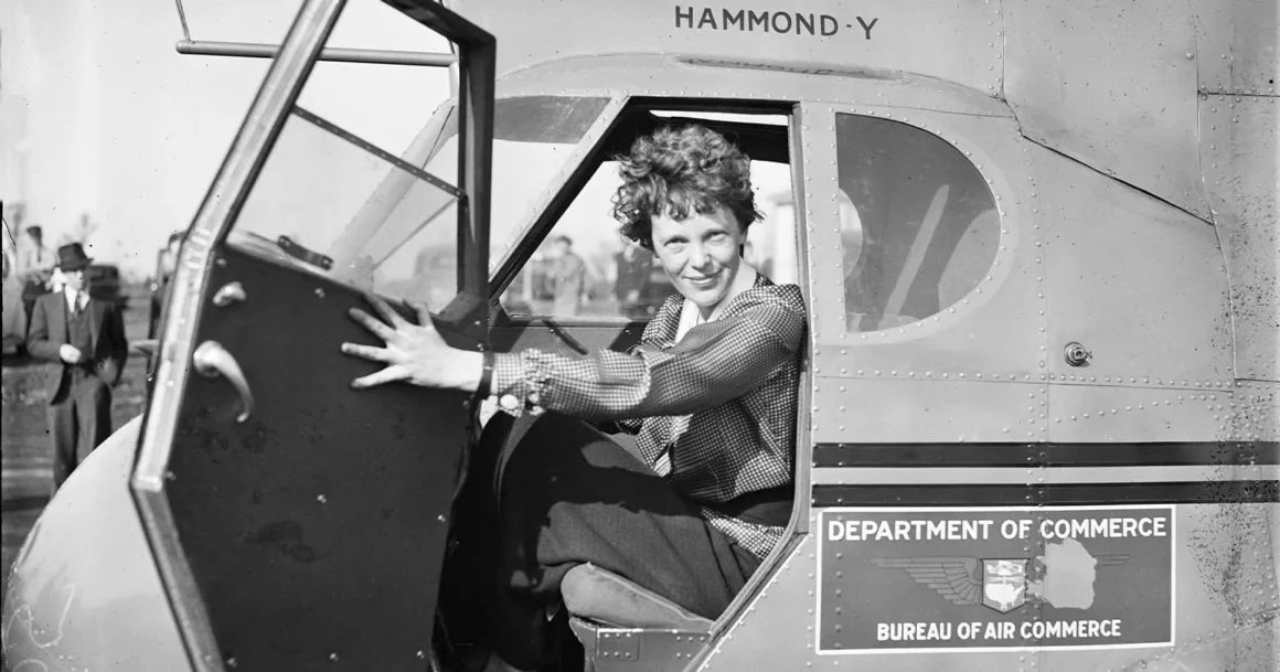 Amelia Earhart’ın Kayıp Uçağı Sanılan Nesne Ağaç Çıktı 1 Amelia Earhart, Hammond Y uçağının kokpitinde açık kapıyı tutarak oturuyor; gövdenin yanında Ticaret Bakanlığı işaretleri görülüyor.