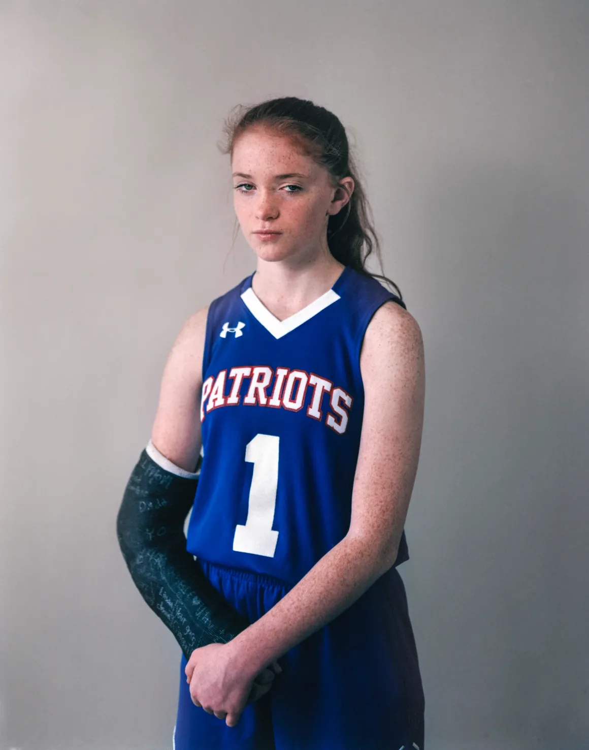 Eva Verbeeck, Amerika’nın Genç Kızlarını 6 Yıl Boyunca Fotoğrafladı 15 Eva Verbeeck, Amerika’nın Genç Kızlarını 6 Yıl Boyunca Fotoğrafladı
Çilleri ve uzun kızıl-kahverengi saçları olan genç bir kız, üzerinde PATRIOTS yazısı ve 1 numarası bulunan mavi basketbol forması giyiyor; sağ kolunda siyah bir alçı bulunuyor.