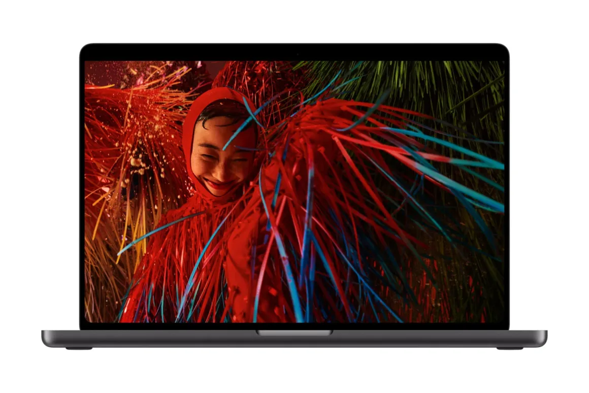 Apple’ın İlk Dokunmatik OLED MacBook Pro’su Tanıtıldı 24 A dark gray laptop is displayed against a white background, showing a vibrant, abstract image of a person wearing a red hood surrounded by colorful, flowing ribbons on its screen.