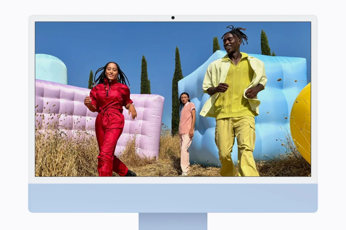 M6 iMac Tanıtıldı: Daha Güçlü Performans, Wi-Fi 7 ve 7 Renk Seçeneği 22 Açık mavi iMac ekranında, büyük renkli şişme yapılar arasında tarlada yürüyen üç kişinin fotoğrafı görülüyor.