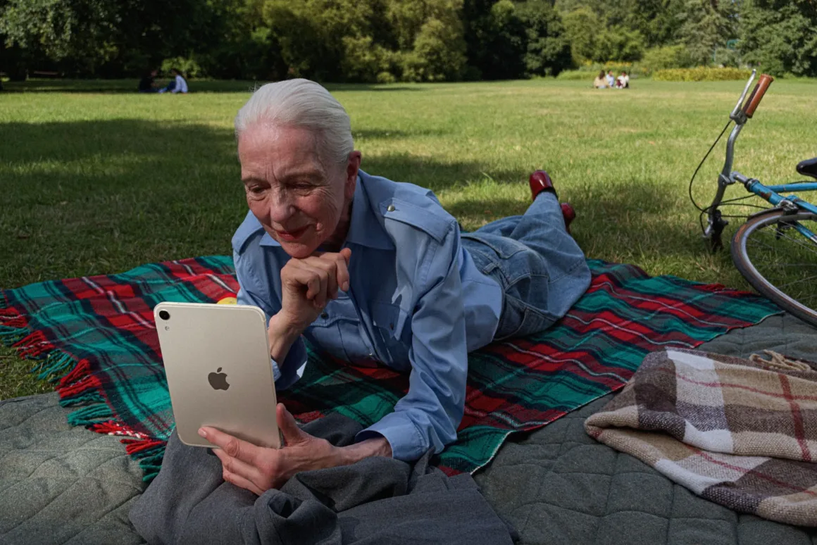 Yeni iPad mini Tanıtıldı: OLED Ekran, A20 Pro ve Daha İnce Tasarım 20 Beyaz saçlı yaşlı bir kadın parkta ekose örtü üzerinde uzanırken elindeki tabletin ekranına bakıyor.