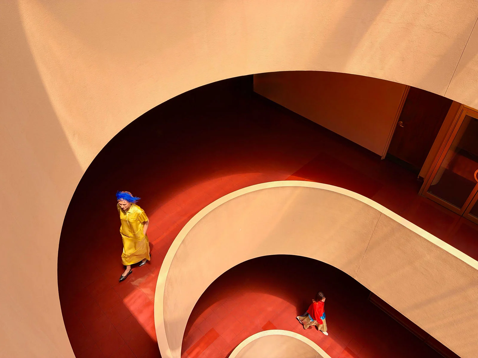 Apple iPhone Duo: İlk Katlanabilir iPhone 7,6 İnç Ekranla Geldi 24 Two people walk along a curved, red-tiled ramp inside a building with beige, circular walls.