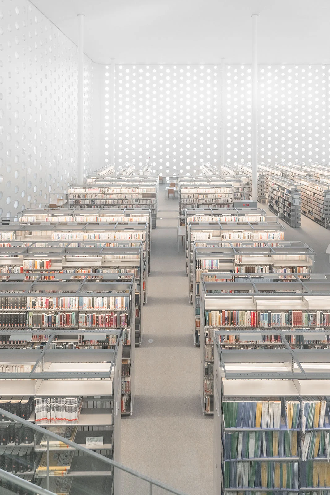 Architecture Photography MasterPrize 2026 Kazananları Açıklandı 19 Tekrarlayan dairesel desenlere sahip duvarların bulunduğu aydınlık ve minimalist bir kütüphanede, kitaplarla dolu yüksek metal raflar sıralanıyor.