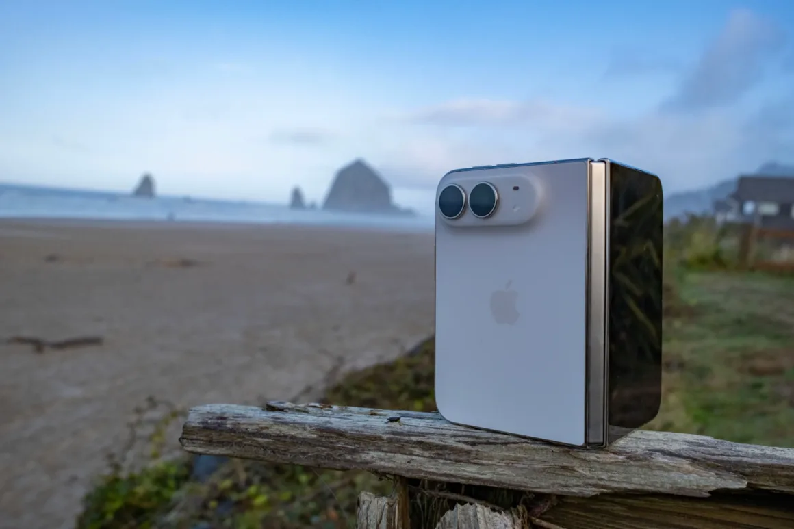 iPhone Duo İncelemesi: Etkileyici Tasarım, Kaçınılmaz Tavizler 38 Çift objektifli kamerası bulunan beyaz katlanabilir akıllı telefon, plaja bakan yıpranmış ahşap bir direğin üzerinde dik duruyor.