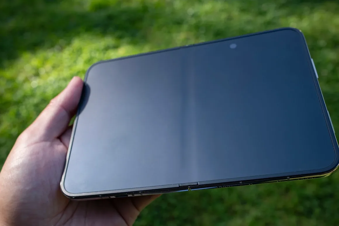 iPhone Duo İncelemesi: Etkileyici Tasarım, Kaçınılmaz Tavizler 20 Bir el, bulanık yeşil çimenlerin önünde tamamen açılmış siyah katlanabilir bir akıllı telefonu tutuyor.