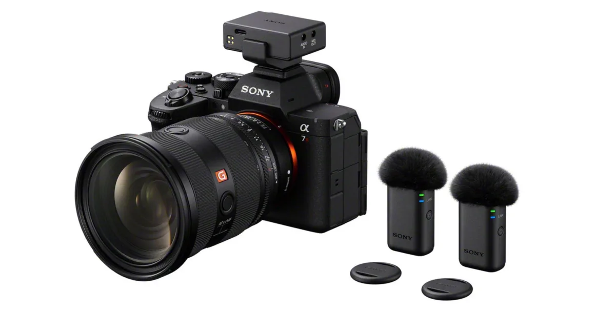 Sony ECM-W5: 32-Bit Float ve 500 Metre Menzilli Kablosuz Mikrofon Sistemi 20 Büyük objektif takılı Sony Alpha 7R fotoğraf makinesinin üzerinde kablosuz mikrofon alıcısı bulunuyor; yanında iki kablosuz mikrofon vericisi ve iki küçük yuvarlak kapak yer alıyor.
