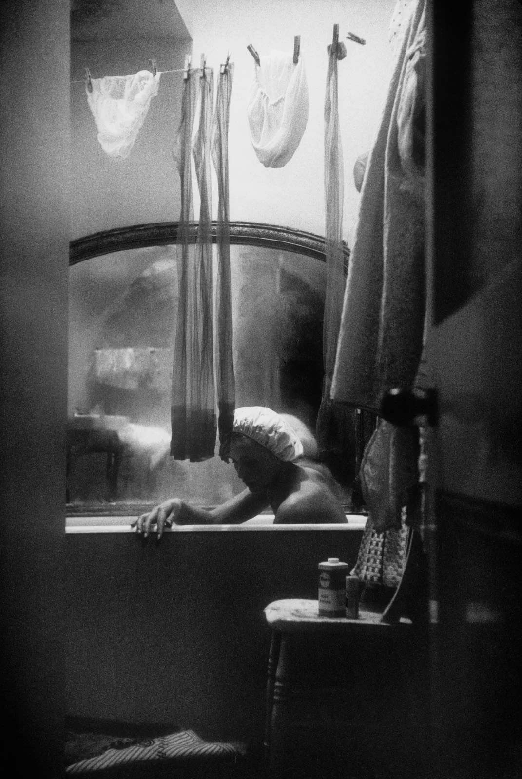 Magnum Fact/Fiction Square Print Sale 26 Ekim’de Başlıyor 24 A person wearing a shower cap sits in a bathtub, viewed through a doorway with laundry hanging on a line above the tub.