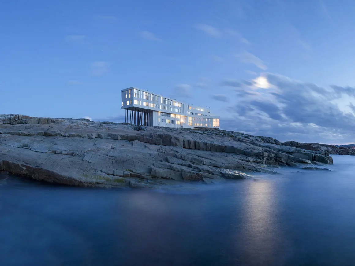 Architecture Photography MasterPrize 2026 Kazananları Açıklandı 37 Çok sayıda penceresi bulunan modern, çok katlı beyaz bina, alacakaranlıkta kayalık kıyı uçurumunun üzerinde ayaklar üzerinde yükseliyor.