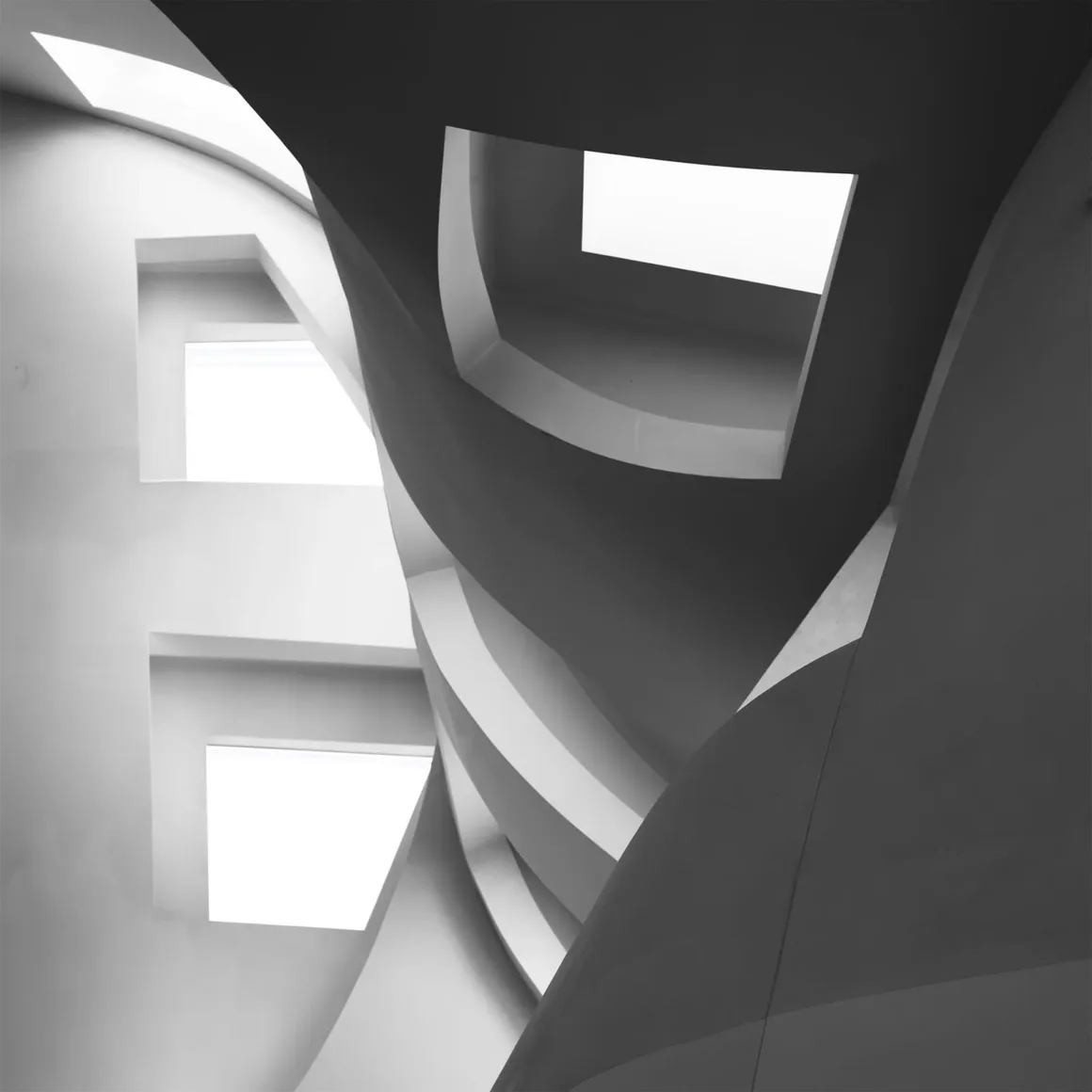 Architecture Photography MasterPrize 2026 Kazananları Açıklandı 38 Modern binanın siyah-beyaz iç görünümünde kıvrımlı heykelsi duvarlar ve dikdörtgen tavan pencereleri görülüyor.