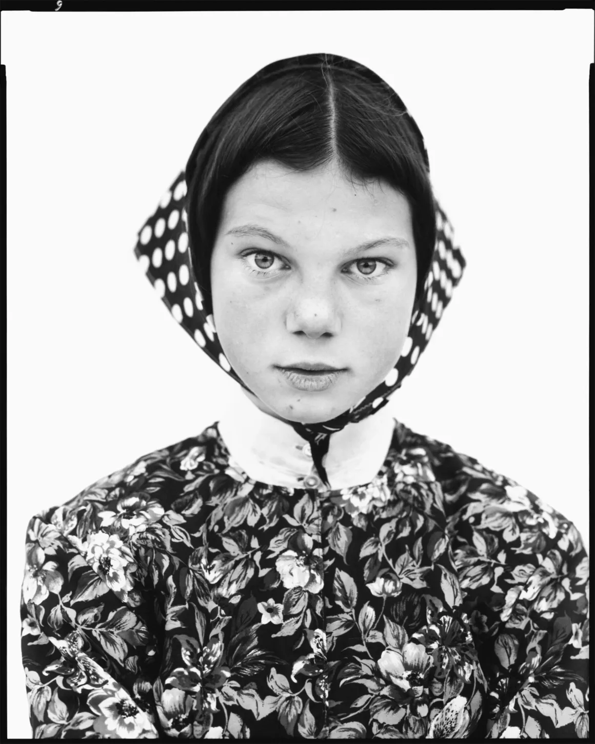 Richard Avedon’ın Amerika’nın Batısına Baktığı Portreler Londra’da 15 Richard Avedon’ın Amerika’nın Batısına Baktığı Portreler Londra’da
Genç bir kız, çiçek desenli elbisesi ve puantiyeli başörtüsüyle kameraya doğrudan bakıyor. Siyah-beyaz görüntü sade beyaz bir fon önünde çekilmiş.