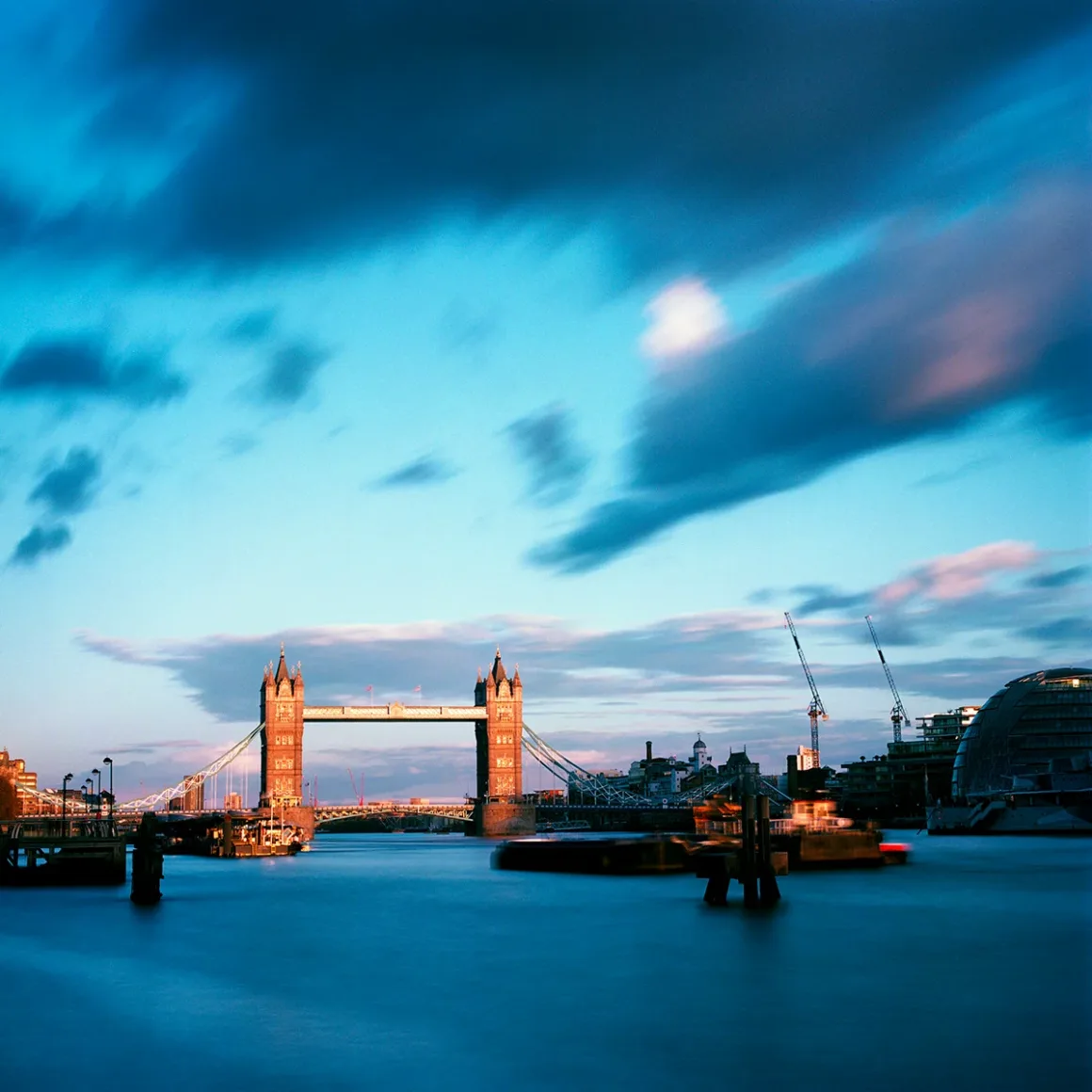 Kodak Portra 160: İnce Grenli Renkli Negatif Filmin Gücü 31 Tower Bridge, alacakaranlıkta bulutlu mavi gökyüzü altında Thames Nehri üzerinde yükseliyor; çevrede inşaat vinçleri görülüyor.