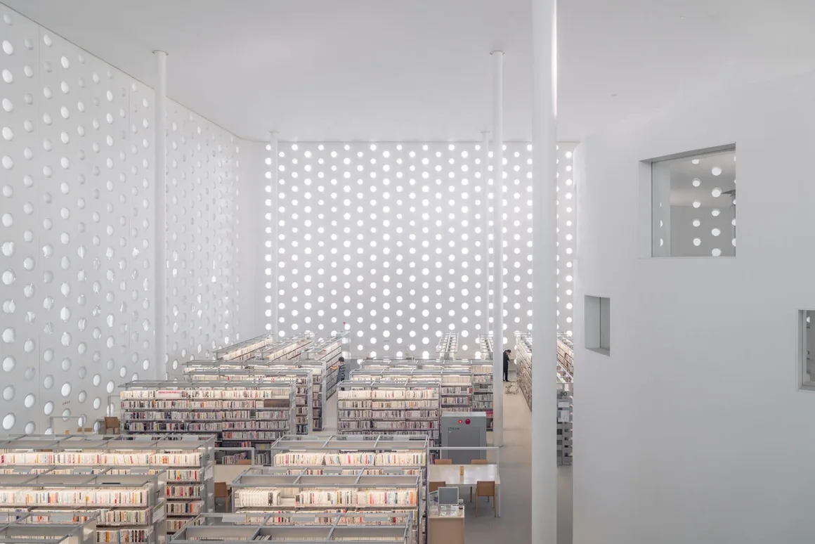 Architecture Photography MasterPrize 2026 Kazananları Açıklandı 21 Yüksek tavanlı, aydınlık ve minimalist kütüphanenin iç mekânında kitap rafları sıralanıyor; duvarlar dairesel açıklıklardan oluşan desenlerle kaplı.