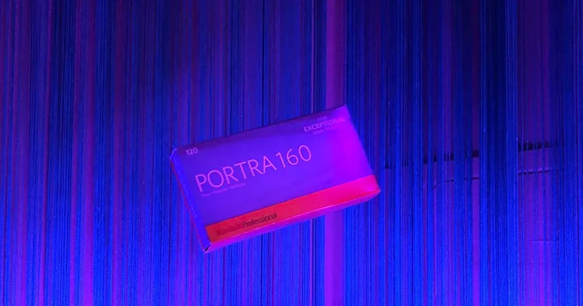 Kodak Portra 160: İnce Grenli Renkli Negatif Filmin Gücü 1 Kodak Professional Portra 160 120 film kutusu, mavi ve mor tonlardaki dikey iplerden oluşan bir arka planın önünde görülüyor.